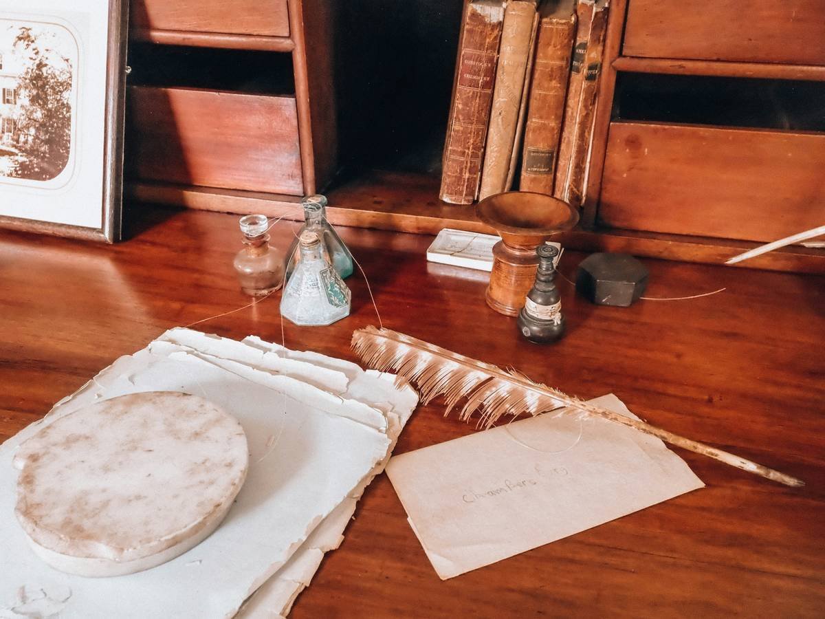 Antique wooden desk with quill pen, old papers, and inkwells.